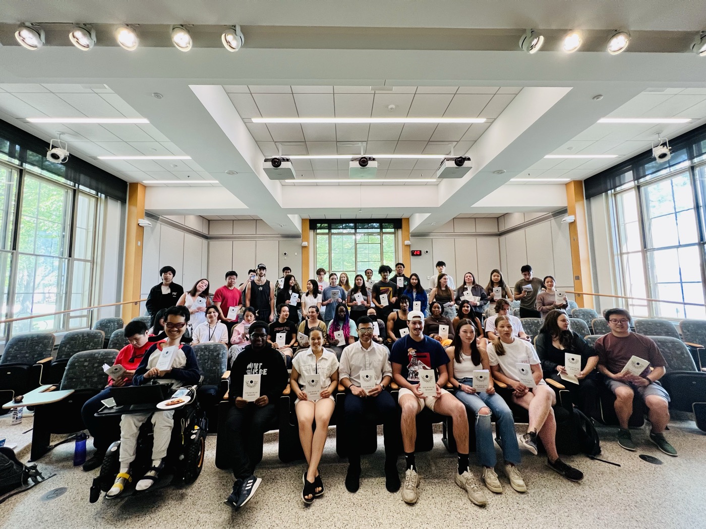 A full lecture hall of students holding up the book their class made together